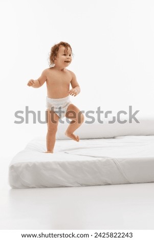 Cheerful little child, small kid, girl with wet hair in standing pose playing on bed against bright white studio background. Concept of childhood, motherhood, life, birth. Copy space for ad