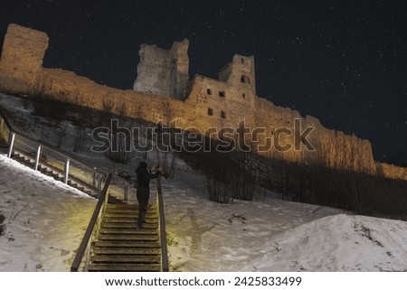 A girl tourist takes pictures on her phone of the ruins of Rakvere Castle in winter at night. High quality photo