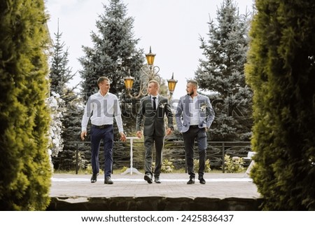 Wedding photography. The groom and his friends are walking against the background of trees, posing. Men in suits. Style. Friendship. Photo session in nature.