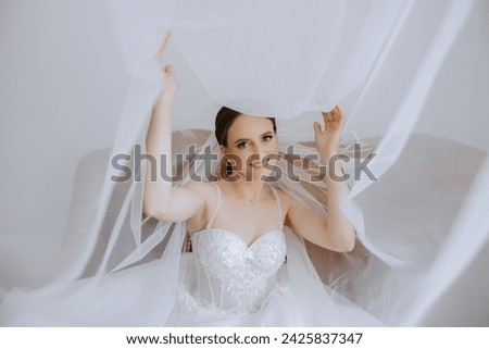 Beautiful young bride holding veil in white wedding dress, portrait of brunette bride in hotel room, morning before wedding.