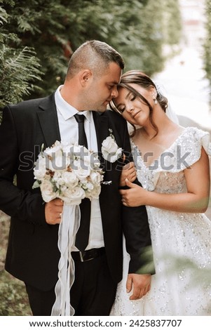 lovely and stylish newlyweds are hugging and smiling against the background of autumn nature in a beautiful garden. An incredibly beautiful young bride leaned against the shoulder of her beloved groom