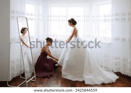 The bridesmaid is happy in the morning, helping to fasten the buttons on the wedding dress and prepare for the wedding ceremony. They take pictures, smile, help the bride with her shoes.