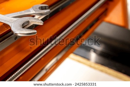 wrenches on a CNC machine are orange, the shaft and guide rails of the machine are visible
 Royalty-Free Stock Photo #2425853331