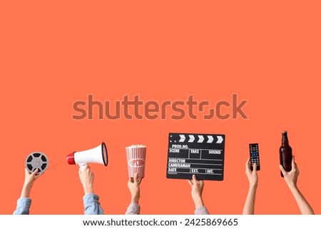 Many hands with bucket of popcorn, movie clapper and beer on orange background