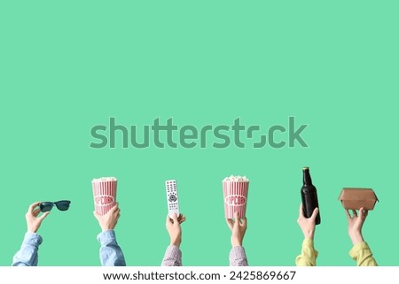 Many hands with buckets of popcorn, beer and TV remote on green background