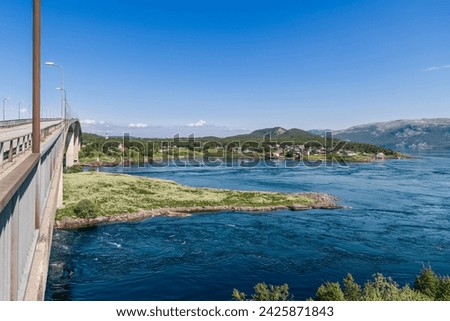 The Saltstraumen Bridge arches over the world's strongest maelstrom, with swirling currents below and a picturesque village in the distance Royalty-Free Stock Photo #2425871843