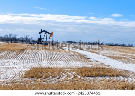 A oil pump jack in an agriculture winter season field with multiple power lines on background