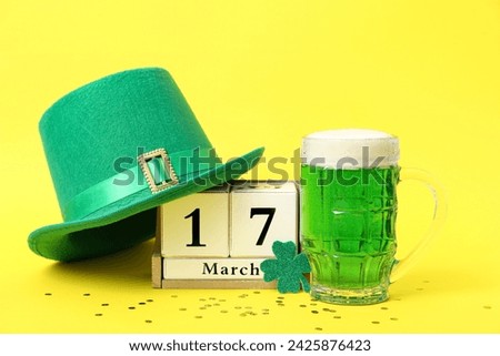 Cube calendar with date 17 MARCH, glass of beer and leprechaun hat on yellow background. St. Patrick's Day celebration