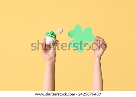 Female hands with tasty cupcake and paper clover for St. Patrick's Day on beige background