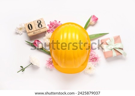 Composition with hardhat, gift box and spring flowers for International Women's Day on white background Royalty-Free Stock Photo #2425879037