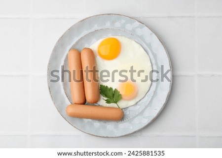 Delicious boiled sausages, fried eggs and parsley on white tiled table, top view