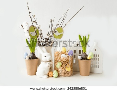 Delicate beautiful festive Easter composition on a light background. Spring flowers, willow twigs, white rabbit, Easter eggs symbol of the holiday. Happy Easter holiday concept. Foreground.

