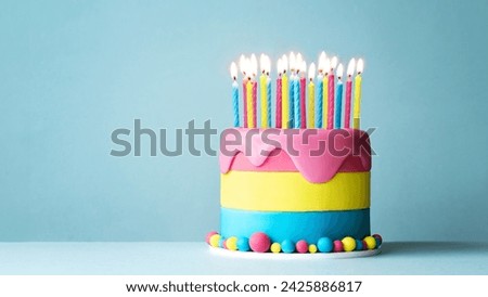 Colorful celebration birthday cake with lots of birthday candles and drip icing against a blue background