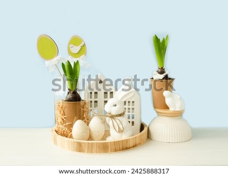Delicate beautiful festive Easter composition on a light blue background. Spring flowers, white rabbit, Easter eggs symbol of the holiday. Happy Easter holiday concept. Front view.

