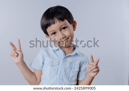 A happy and smiling Asian boy showing peace sign in studio portrait. Indonesian boy wearing casual outfit isolated over white background
