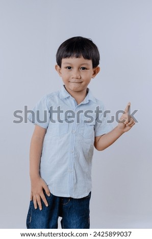 A happy and smiling Asian boy showing first finger sign in studio portrait. Indonesian boy wearing casual outfit isolated over white background