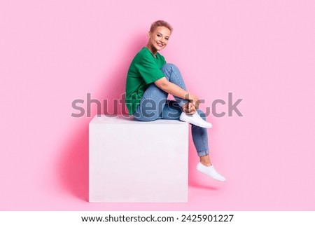 Full size side profile photo of nice girl dressed green t-shirt sit on white cube on black friday isolated on pink color background