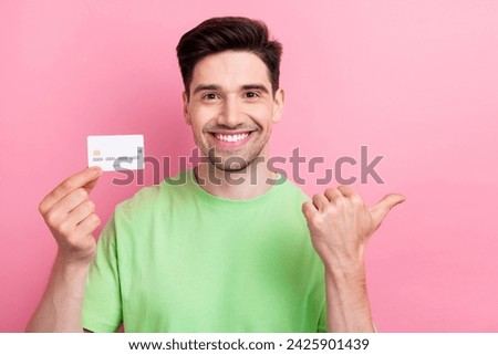 Photo of young cheerful businessman wearing green t shirt pointing finger empty space credit card ads isolated on pink color background