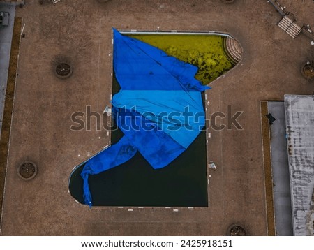 A top down drone view over a partially covered pool on a cloudy day. The pool is filled filthy with green, dirty water. Royalty-Free Stock Photo #2425918151