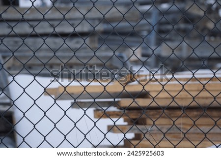 Fastened pile of timber planks on snowy ground, chainlink fence in foreground  Royalty-Free Stock Photo #2425925603