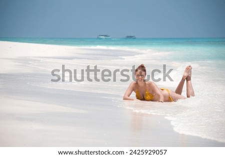 Beautiful happy woman in yellow swimsuit laying on a white sand beach in the water at the sea. Smiling girl in bikini resting during summer vacation at the seashore. Asia vacation.