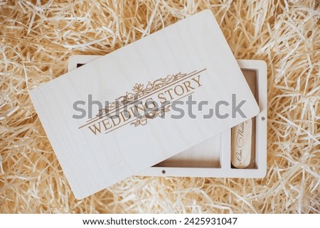 Wooden photo box for photo storage on straw background. Open Box with flash with laser engraving "wedding story" set for the photographer, presentable set of photos, luxury feedback to client. Royalty-Free Stock Photo #2425931047