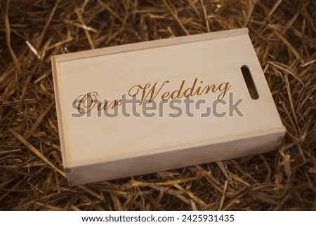 Wooden photo box for photo storage on straw background. Box with flash with laser engraving "Our wedding" set for the photographer, presentable set of photos, luxury feedback to client. Royalty-Free Stock Photo #2425931435