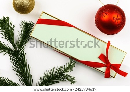 Beautiful gift box in pastel green and gold, wrapped with a red ribbon, on a white background. There are some spruce and Christmas decorations, and copy space.