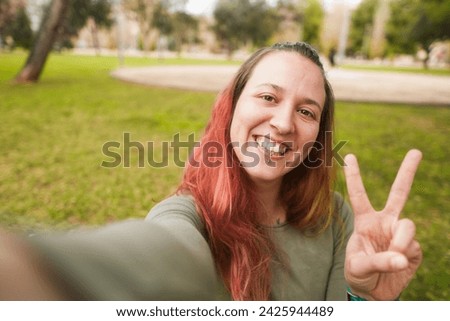 Woman taking a selfie with a peace sign in the park.