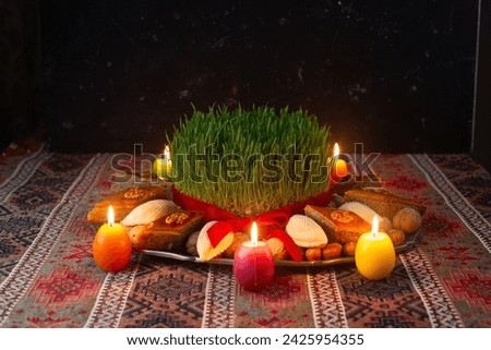 Beautiful Novruz tray on rug with semeni - wheat grass, pakhlava, shekerbura and festive candles on national Azerbaijani carpet table cloth. Spring equinox and new year celebration in Baku.