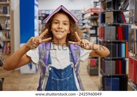 Portrait of happy girl child with opened diary on head gesturing peace sign