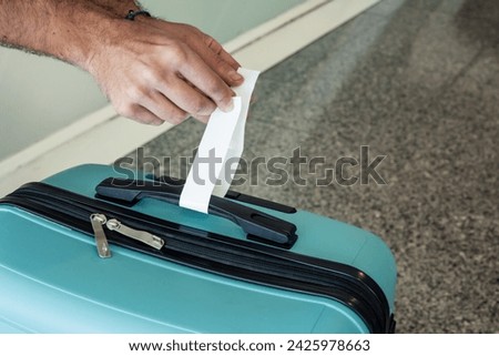 closeup hand putting checked luggage sticker to blue suitcase at airport security check before flight