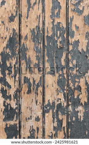 Vertical photo of an old wooden boards painted with dark paint, which has partially peeled off due to time and weather conditions