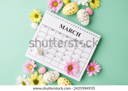 Countdown to Easter: blooms and bunnies setting the scene. Top view photo of March calendar, white ceramic bunny, colorful Easter eggs surrounded by chrysanthemums on teal background