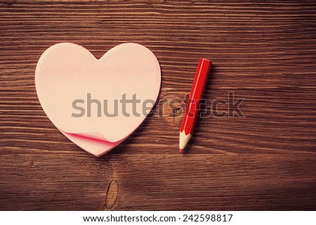 Sticky notes in the form of hearts and red pencil on vintage wooden background