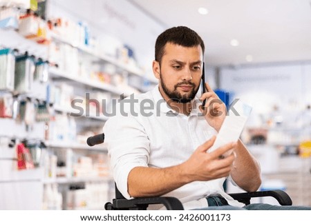 Man in a wheelchair consults on a mobile phone about buying medicine in a pharmacy