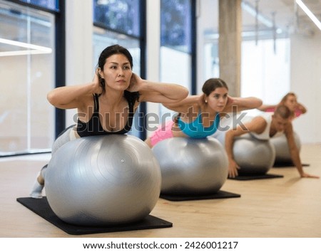 Adult sports people practiciting Pilates in the studio during a group training session perform an exercise on a fitness ball, ..which strengthens the lumbar region and develops overall flexibility Royalty-Free Stock Photo #2426001217