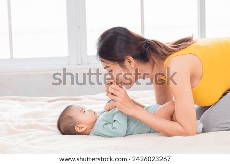 Beautiful Asian mother holding baby hand, baby looking female eye contact. Touching of love bonding relationship between mom and child concept, infant and mother spend time together at home. Royalty-Free Stock Photo #2426023267