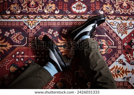 Close-up view of two-tone wingtip brogue shoes made of genuine leather worn indoors on the classic red carpet. Concept photo of classic wingtip brogue shoes with a red Turkish carpet base