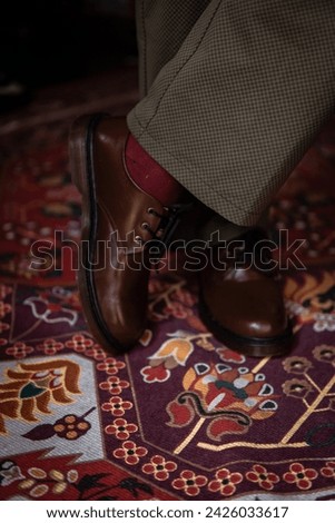 Close-up of 3-hole boots made of genuine leather worn indoors on the classic red carpet. Formal indoor concept photo with brown boots on Turkish red carpet