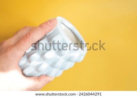 Man's hand holds a light blue massage roll on a yellow background.