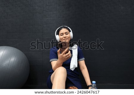 A confident woman with a leg prosthesis and wearing headphones sits on the floor listening to her smartphone's music. after exercising at the gym
