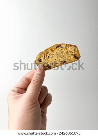 Hand holding a piece of almond cranberry Biscuit. Dry sweet and tasty bakery food. Object photography isolated on studio white background.