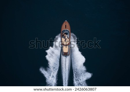 Classic Italian wooden boat fast moving aerial view. Luxurious wooden boat fast movement on dark water. A large modern high-speed wooden luxury boat. Top view of a wooden powerful motor boat. Royalty-Free Stock Photo #2426063807