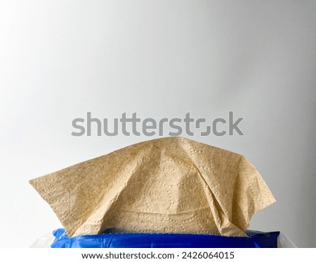 Brown textured tissue paper with subtle flower pattern design coming out from original plastic packaging. Object photography isolated on white plain studio background.