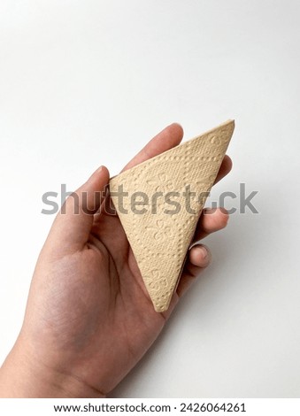 Hand holding One folded triangle brown textured tissue paper with subtle flower pattern. Object photography isolated on white plain studio background.