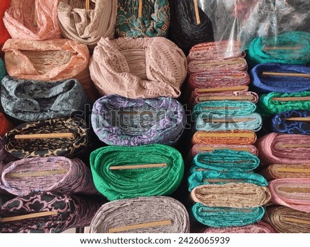 rolls of fabric in a variety of designs and colors, organized neatly in the shop area; this fabric will be utilized as the primary material for clothing and other creative works in the future.