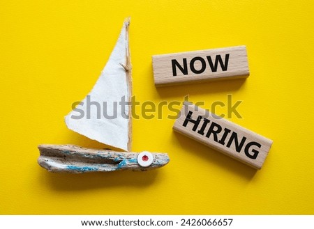 Now Hiring symbol. Concept word Now Hiring on wooden blocks. Beautiful yellow background with boat. Business and Now Hiring concept. Copy space