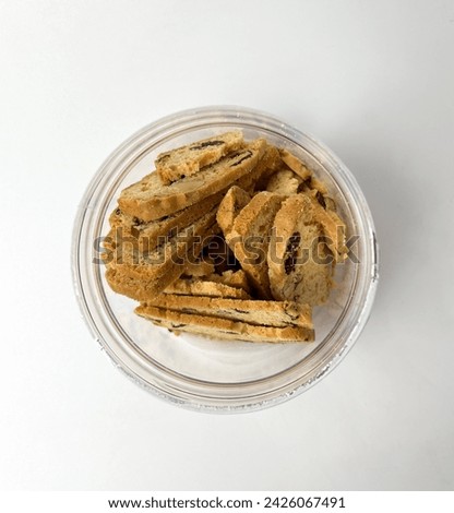 Almond cranberry Biscuits inside clear plastic container jar from top view and opened lid. Dry sweet and tasty bakery food. Object photography isolated on studio white background.