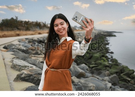 Pretty young latina asian woman smiling taking a selfie with a mobile phone in Jersey shore, she is outdoors natural lights Royalty-Free Stock Photo #2426068055